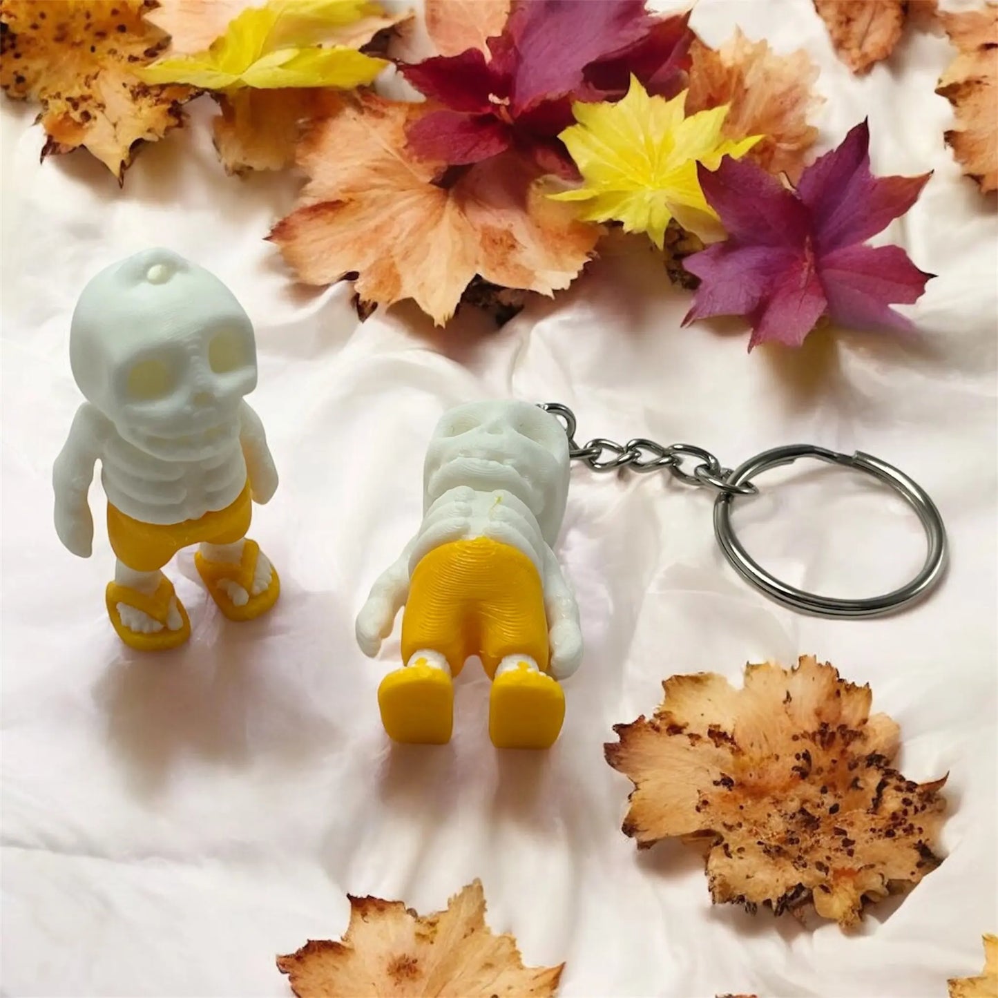Two skeleton keychains with yellow shoes on a white surface with autumn leaves.